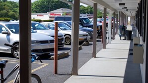 A covered parking area with multiple cars parked, a bicycle, and a visible pharmacy sign in the background. - Travel Inn (North Kingstown)