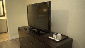 A dark wooden dresser with a flat-screen TV on top, a remote control, and a tray with tissues and a box. - Travel Inn (North Kingstown)