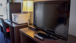 A hotel room with a TV, a lamp, a microwave, and a remote control on a wooden table. - Travel Inn (North Kingstown)