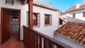 A residential building with a tiled roof, wooden balcony railing, and a door leading to a kitchen area. - SUITES CASA DE LAS COLUMNAS (Granada)
