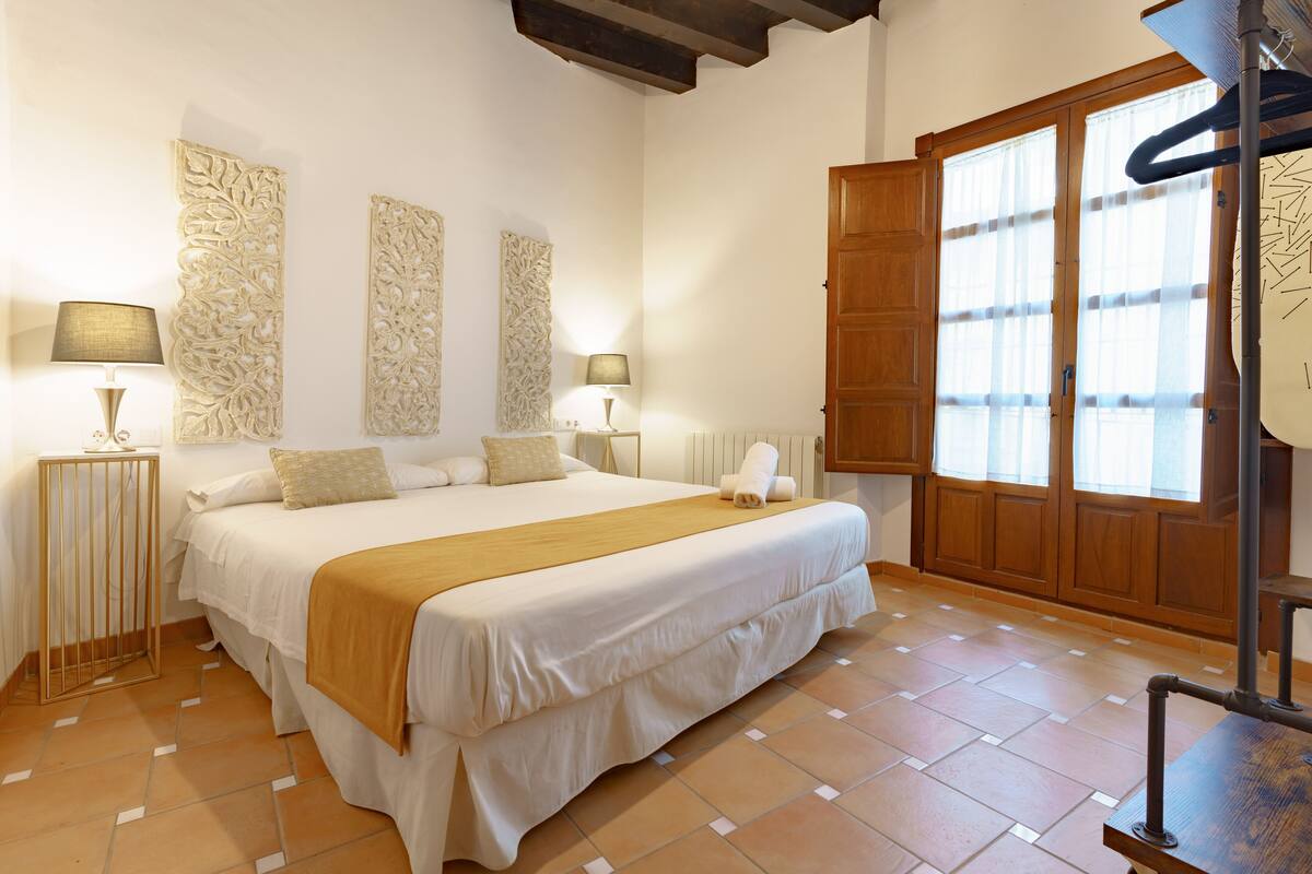 A bedroom with a large bed, two bedside lamps, decorative wall panels, a wooden door, and a tiled floor.