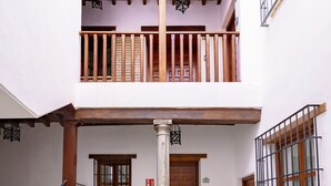 A courtyard with a tiled floor, a wooden staircase, a potted plant, and a door with a window. - SUITES CASA DE LAS COLUMNAS (Granada)