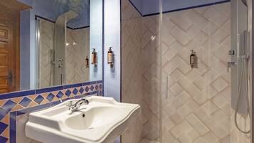 Un baño con un lavamanos blanco, una mampara de ducha de vidrio y una pared de azulejos con diseño de rombos.