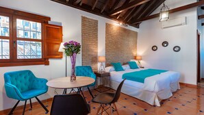 A room with a bed, a table with chairs, a window, and a brick wall. - SUITES CASA DE LAS COLUMNAS (Granada)