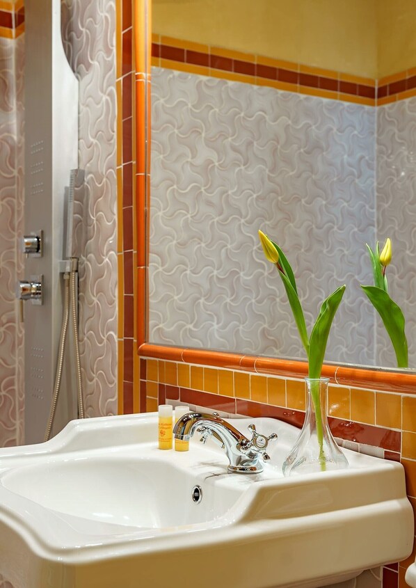 A bathroom with a white sink, a glass vase with green leaves, and a shower with a wavy tile pattern. - SUITES CASA DE LAS COLUMNAS (Granada)
