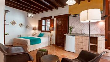 Un dormitorio con cama, mesitas de noche, un escritorio y una silla. Hay una kitchenette con refrigerador, lavaplatos y encimera.