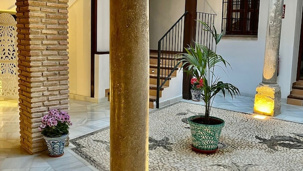A spacious courtyard with a central column, potted plants, and a tiled floor. - SUITES CASA DE LAS COLUMNAS (Granada)
