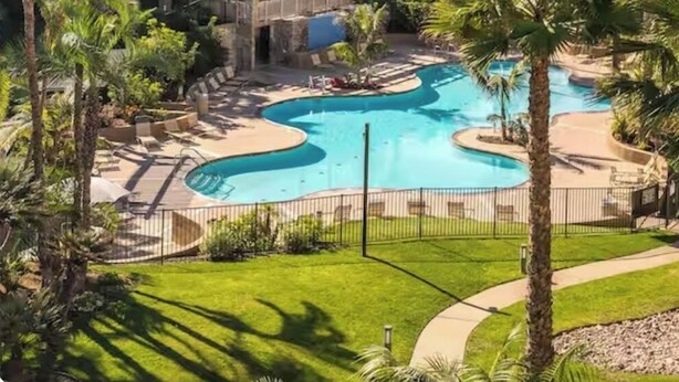 A resort with a pool, palm trees, and a building with balconies. - Pearl on the Strand - Ocean and Village Views at Oceanside Beach! (Oceanside)