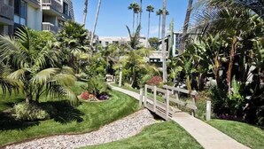 A resort with a pathway, palm trees, and a white fence. - Pearl on the Strand - Ocean and Village Views at Oceanside Beach! (Oceanside)