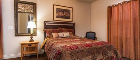 A bedroom with a wooden bed, a nightstand, a lamp, a framed picture, and a window with curtains.