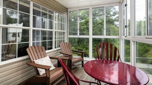 A sunroom with large windows, wooden chairs, a red table, and a ceiling fan. - Lakeside Condo on Lake Taneycomo (Branson)