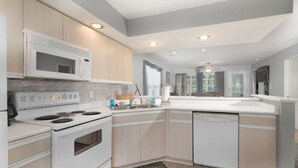 A modern kitchen with white appliances, light wood cabinets, and a large window providing natural light. - Lakeside Condo on Lake Taneycomo (Branson)