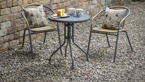 A round metal table with two wicker chairs, each with patterned cushions, set against a brick wall on a gravel surface. - Hope Cottage - UK40055 (Aberfeldy, near Pitlochry)
