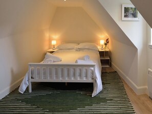 A bedroom with a white bed, two bedside lamps, a framed picture on the wall, and a green striped rug.