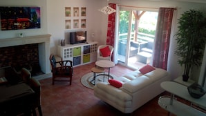 A living room with a white sofa, a dining table, chairs, a TV, and a fireplace. - Beautiful view over the heights of Sarlat in a quiet, not overlooked location with air-conditioned swimming pool. (Sarlat-la-Canéda)