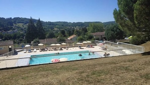 A swimming pool with lounge chairs and umbrellas, surrounded by a fence, set against a hillside backdrop. - Beautiful view over the heights of Sarlat in a quiet, not overlooked location with air-conditioned swimming pool. (Sarlat-la-Canéda)