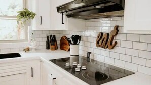 Una cocina con armarios blancos, una estufa negra y un salpicadero con baldosas blancas.