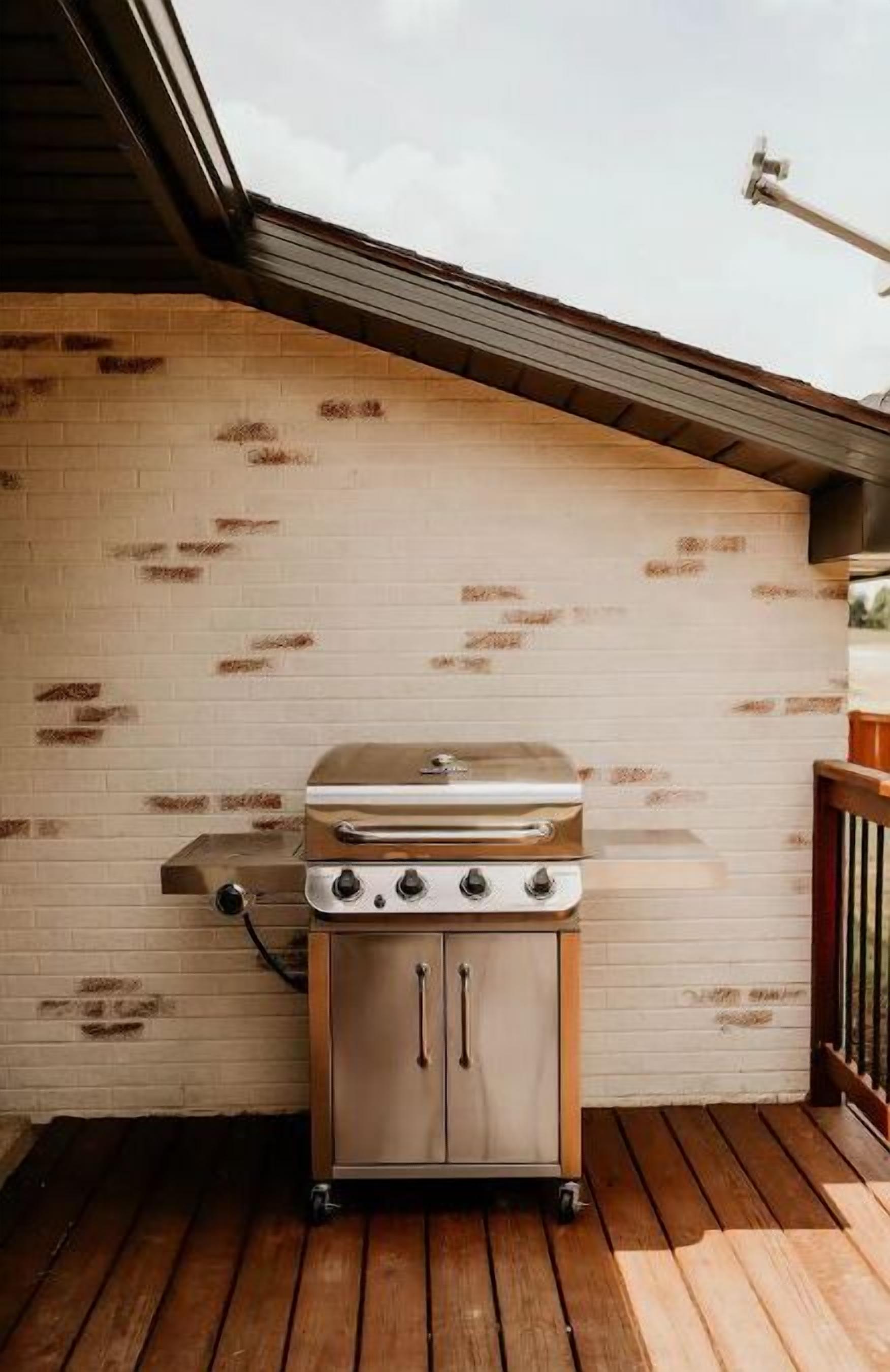 Un barbecue au gaz portatif installé sur une terrasse en bois, avec un mur de briques en arrière-plan.