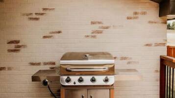 Un barbecue au gaz portatif installé sur une terrasse en bois, avec un mur de briques en arrière-plan.