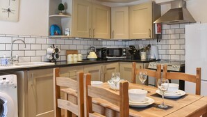 A modern kitchen with beige cabinets, a black countertop, and a dining area with wooden chairs and a table set for two. - 2 bedroom accommodation in Hawes (Hawes)