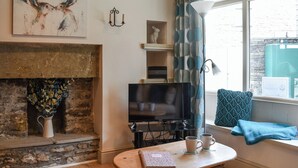 A cozy living room with a fireplace, a flat-screen TV, and a window with curtains. - 2 bedroom accommodation in Hawes (Hawes)