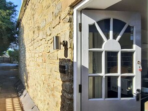 Ein Steinhaus mit einer weißen Tür, einem Metallbriefkasten und einem Fenster mit Fensterläden.