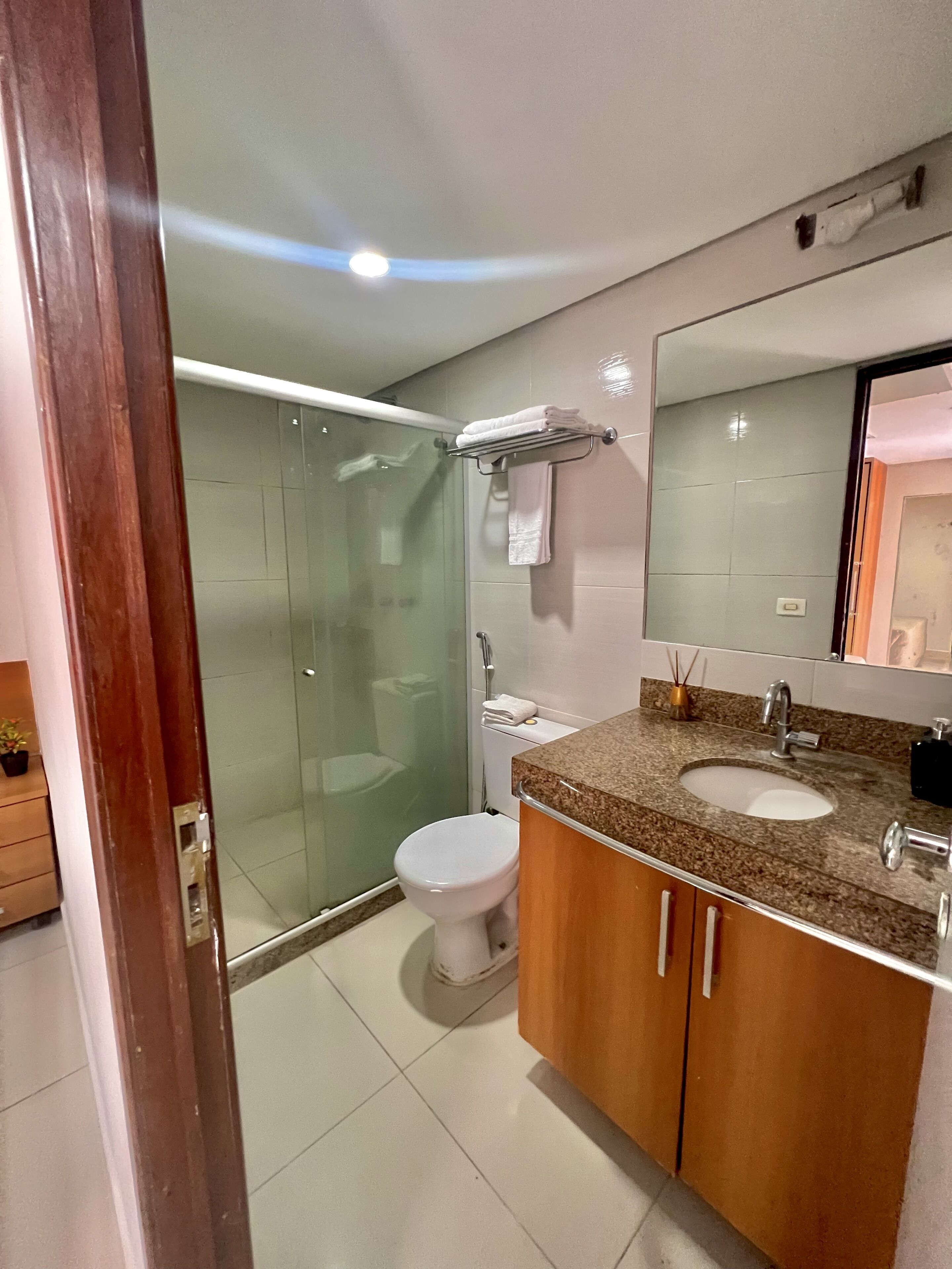 Un baño moderno con cabina de ducha de vidrio, inodoro blanco, lavamanos con encimera de granito y armarios de madera.
