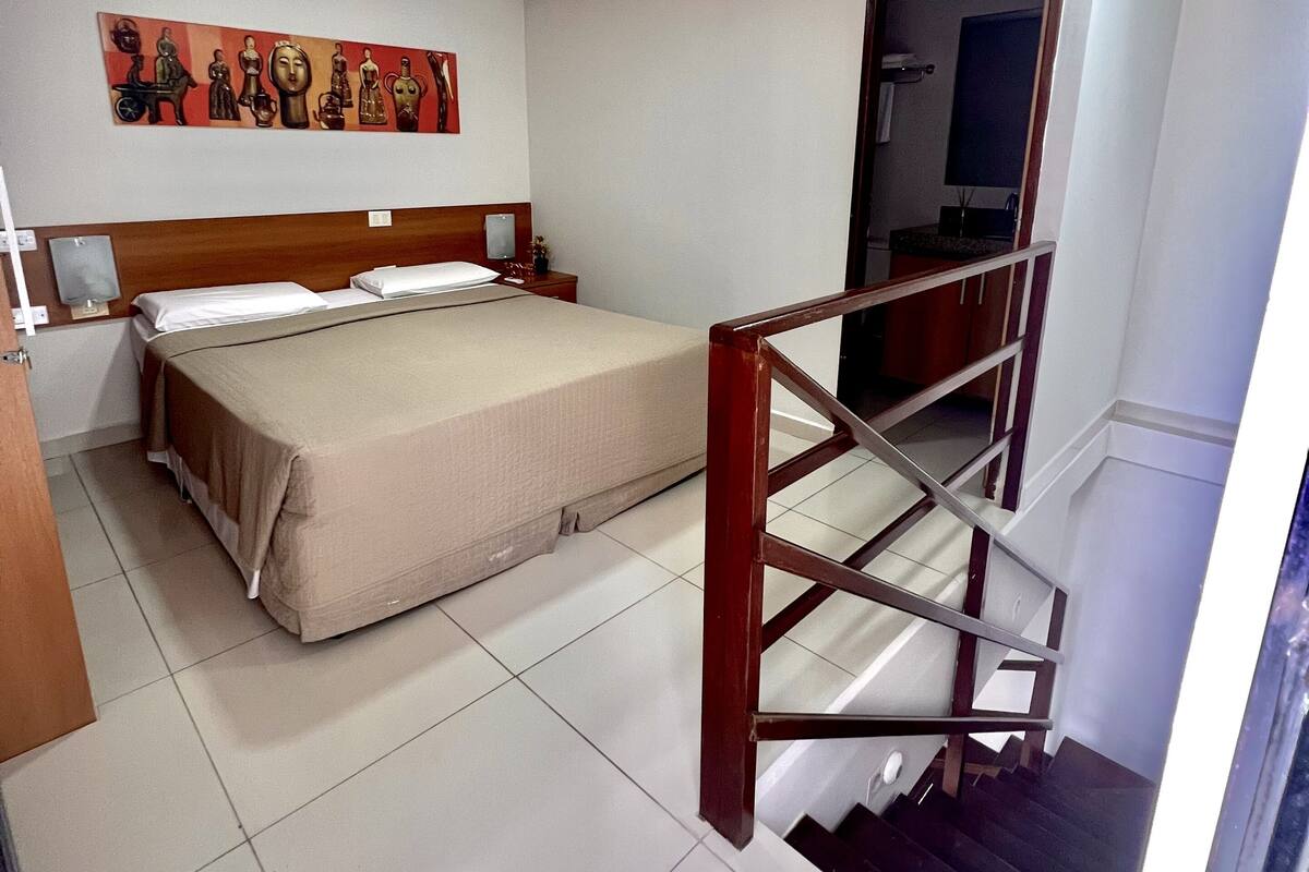 Ein Hotelzimmer mit Bett, einem Bild an der Wand, einem Holzkopfteil, einem Nachttisch und einer Treppe.