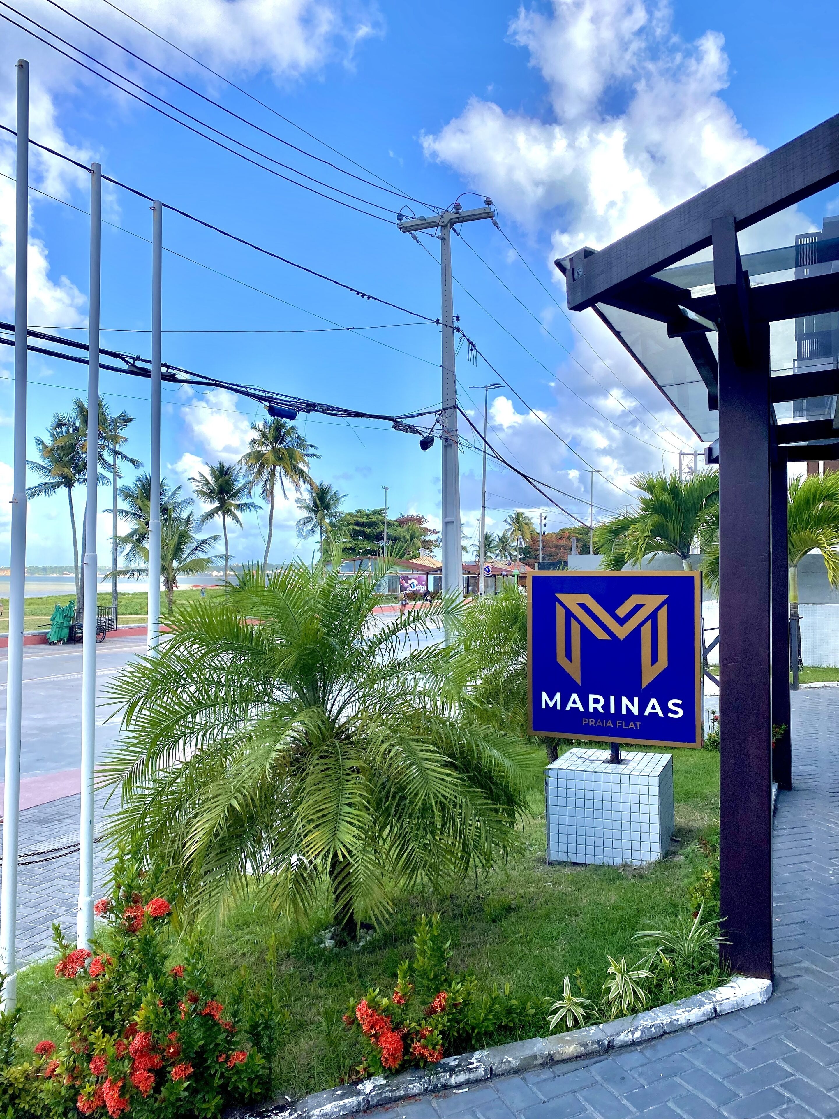A sign for "MARINAS PRAIA FLAT" with a modern building structure and palm trees in the background.