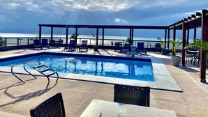A rooftop pool with a view of the ocean, surrounded by lounge chairs and a pergola. - MARINAS PRAIA FLAT (João Pessoa)