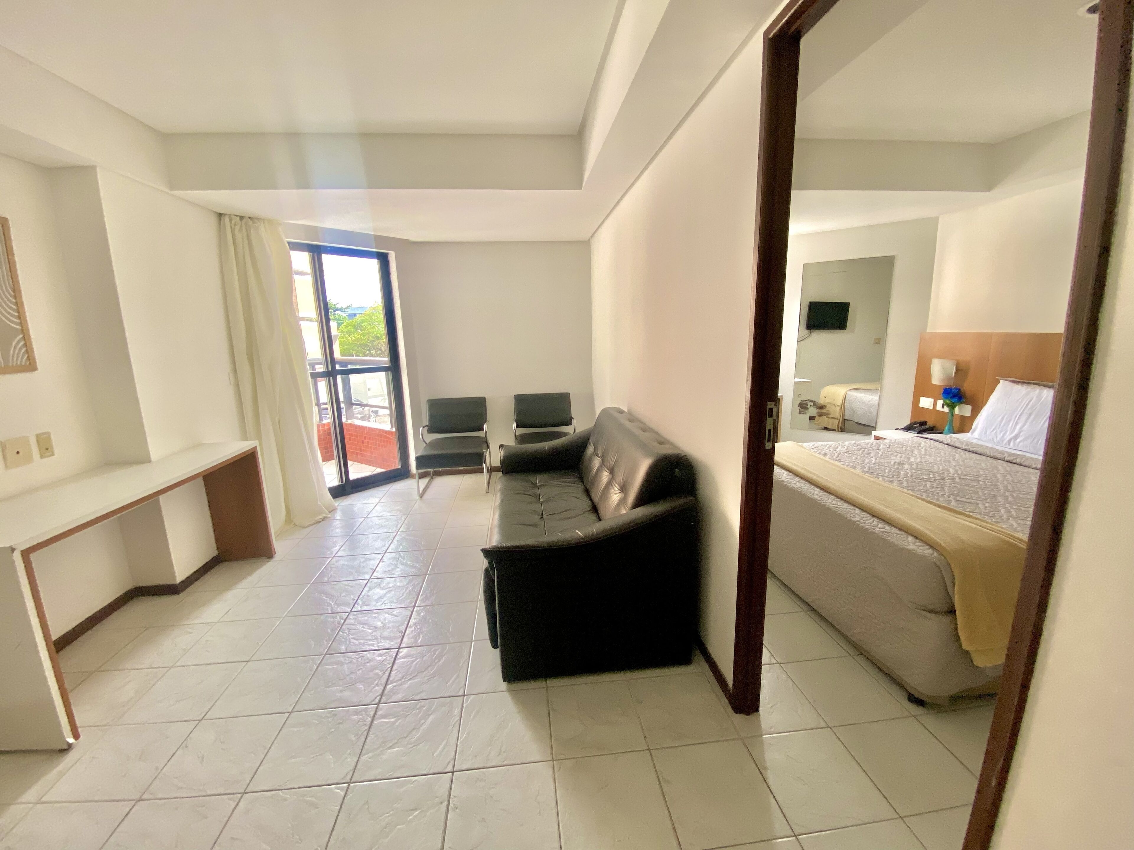 Une chambre d’hôtel avec un lit, un canapé en cuir noir, un petit bureau et une chaise.