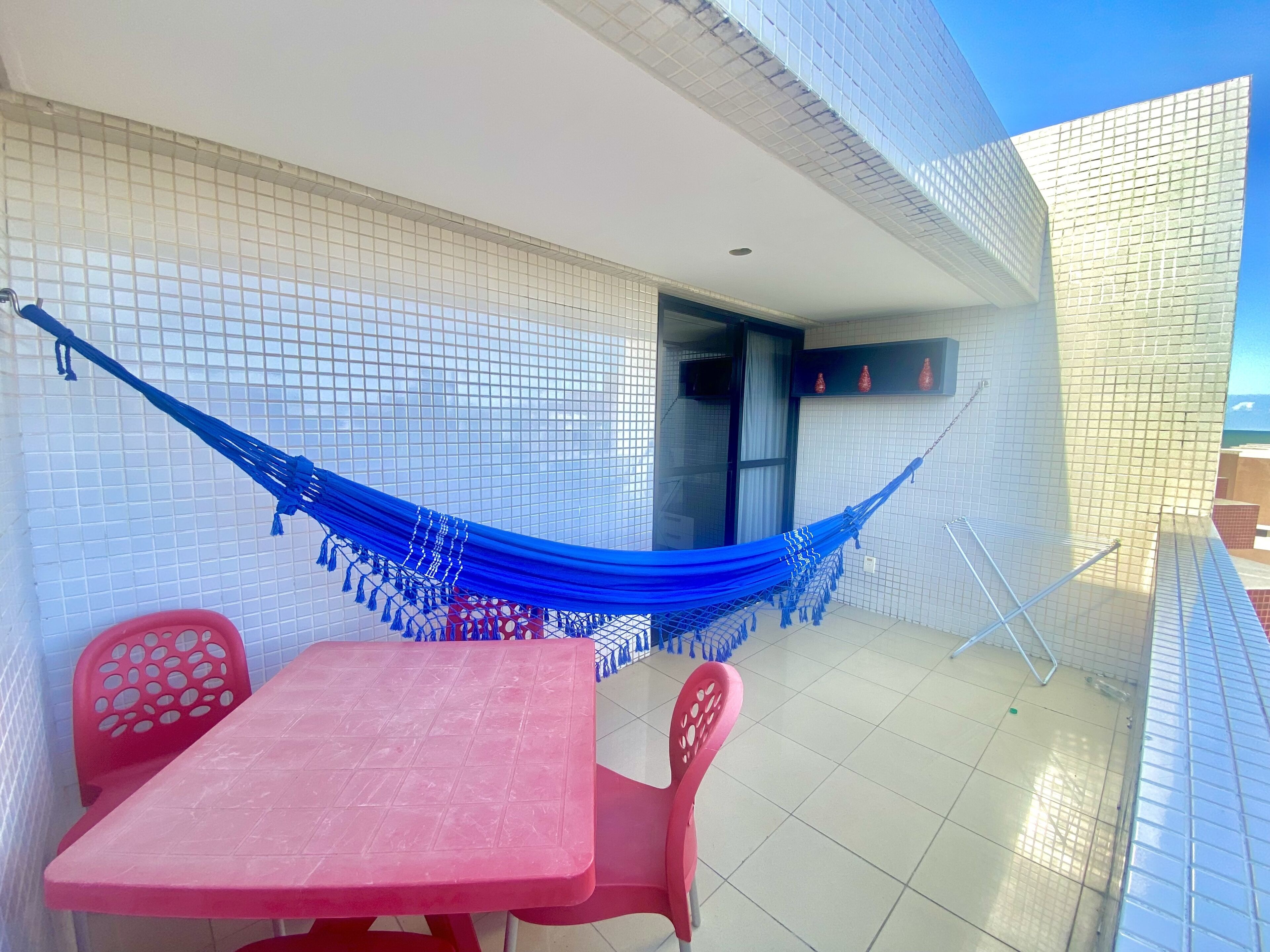 Een balkon met een blauwe hangmat, een rode tafel en bijpassende stoelen.