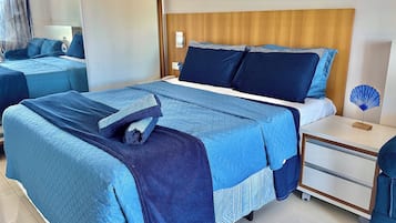 Quarto de hotel com uma cama grande, uma mesinha de cabeceira e um criado-mudo.