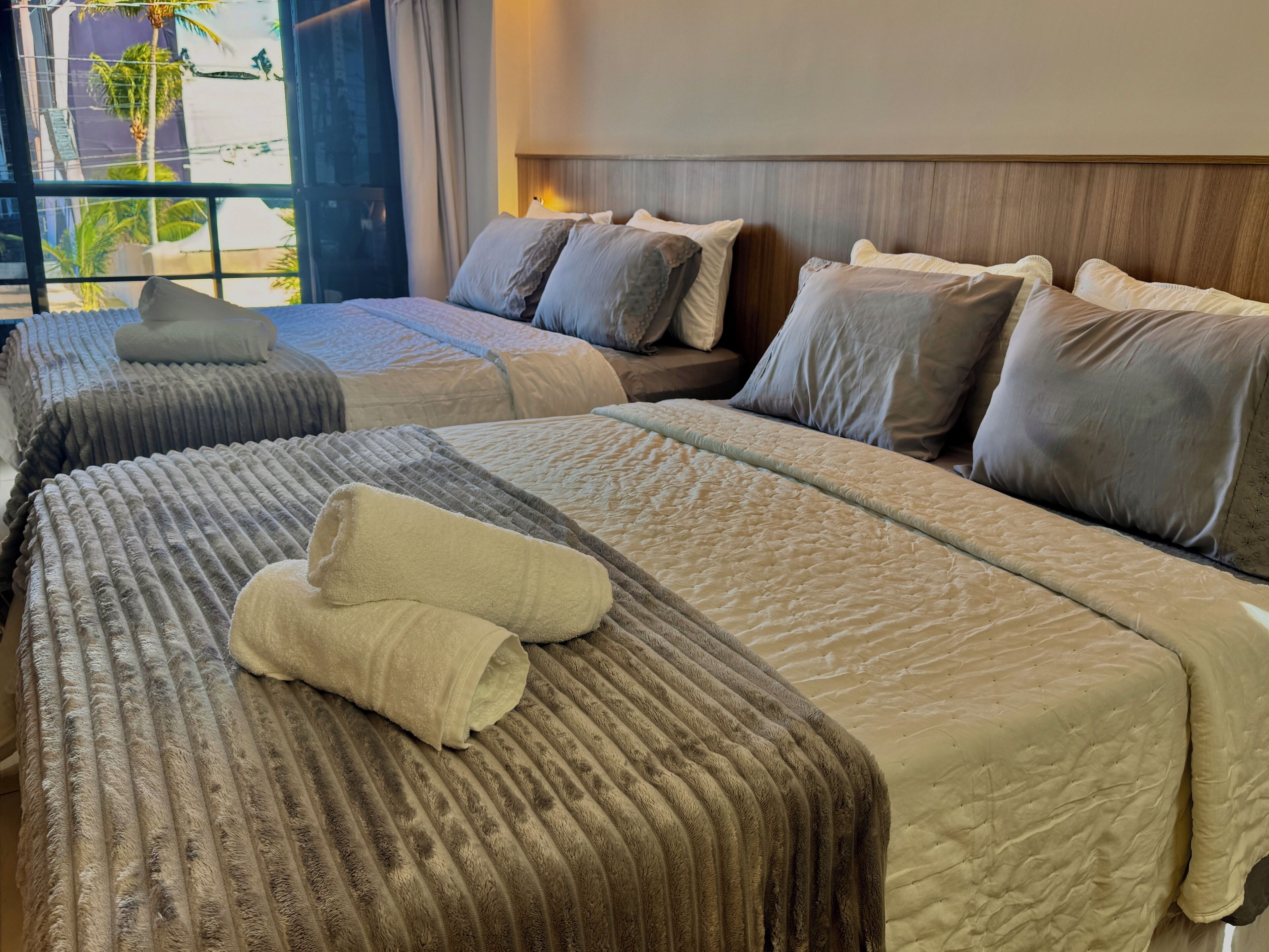 A hotel room with two beds, each with a headboard, and a large window with a view of palm trees.