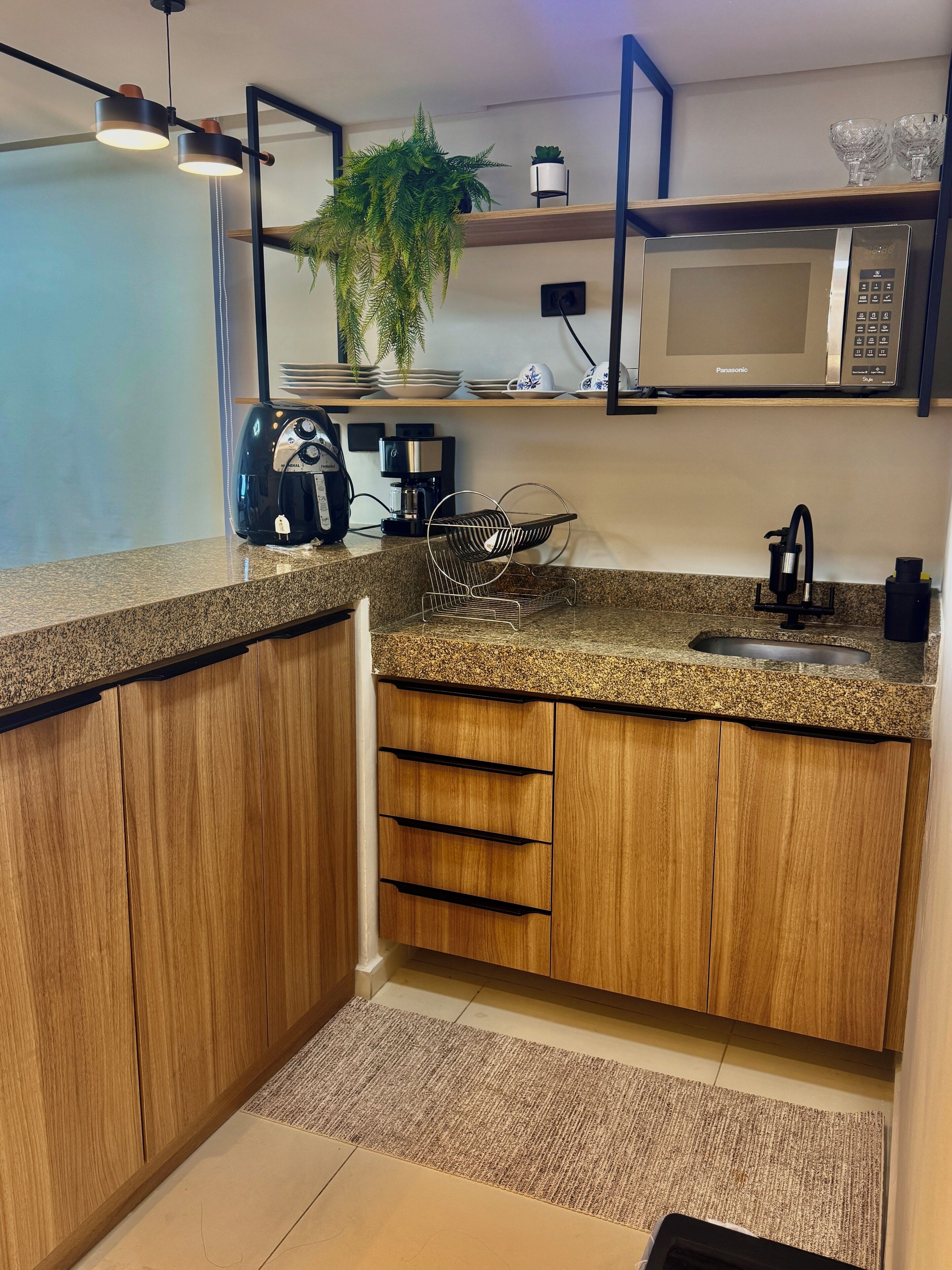 Une cuisine moderne avec des meubles en bois, un plan de travail en granit, un four à micro-ondes encastré, une machine à café et une plante.