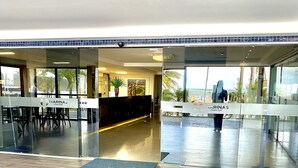 A modern reception area with a reception desk, seating area, and a view of the ocean. - MARINAS PRAIA FLAT (João Pessoa)