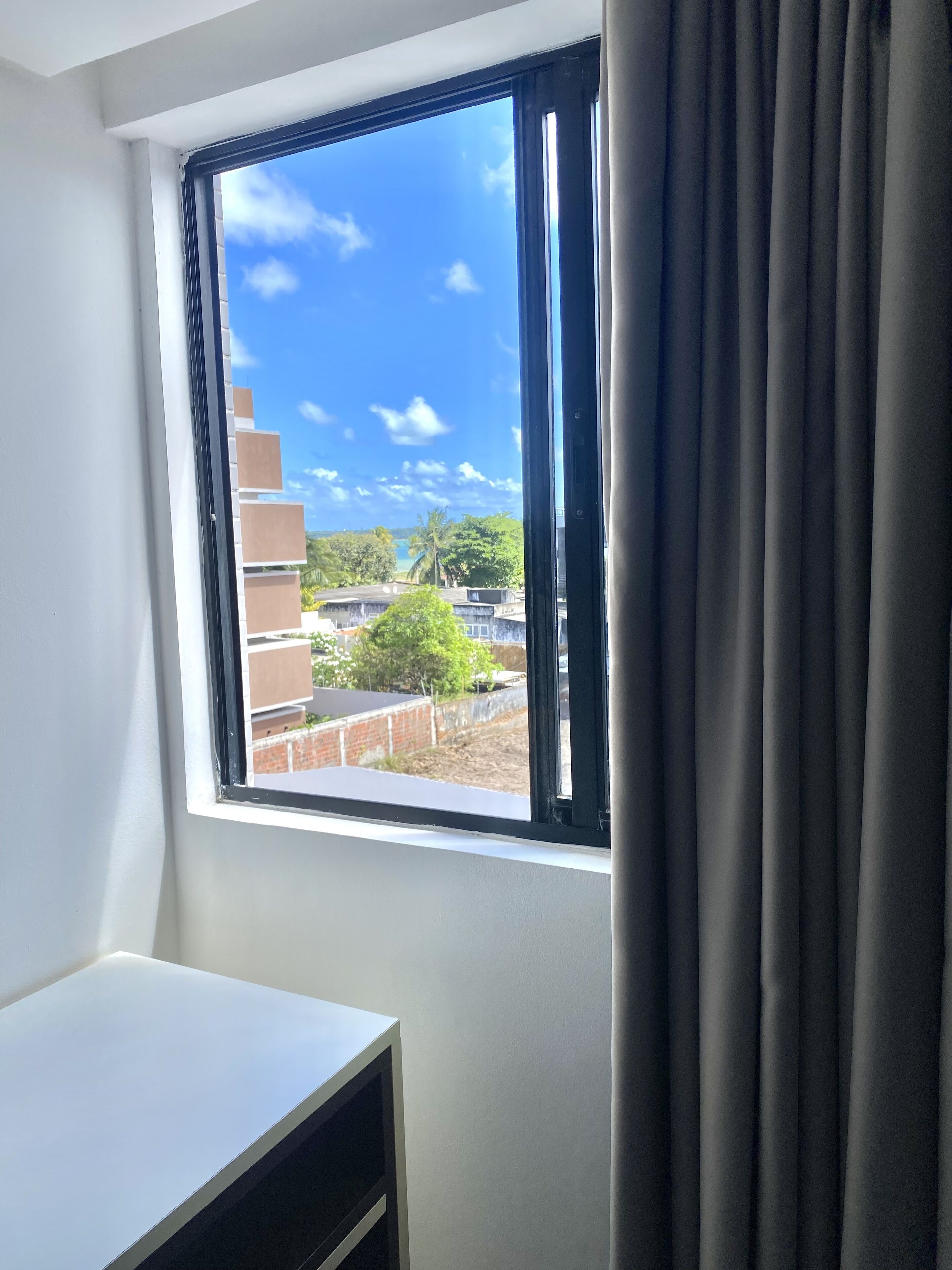 Ein Zimmer mit Fensterblick auf eine Wohngegend, einem weißen Schreibtisch und einem Vorhang.