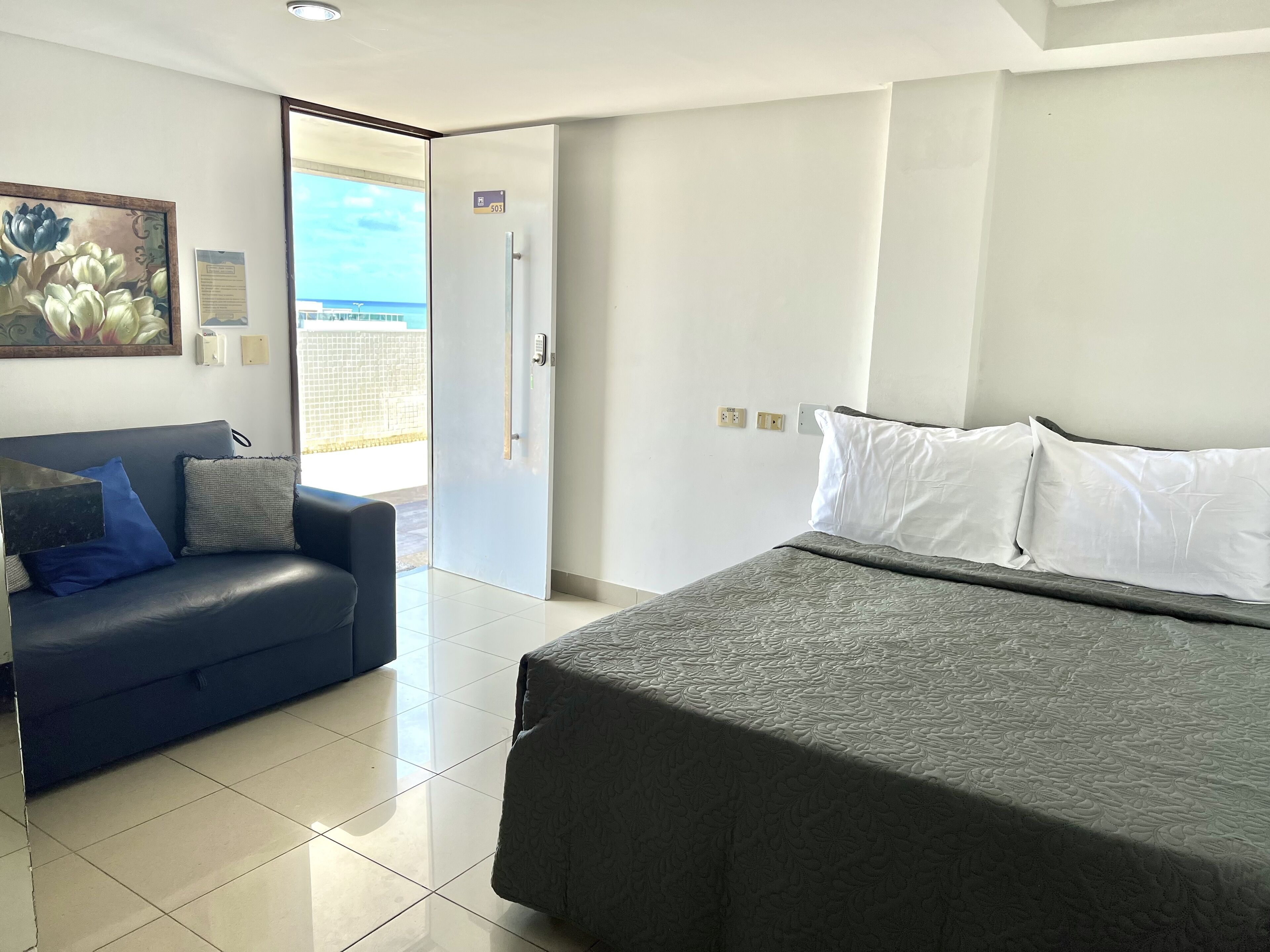 Ein Hotelzimmer mit einem Bett, einem Sofa, einer Tür zu einem Balkon und einem Gemälde an der Wand.