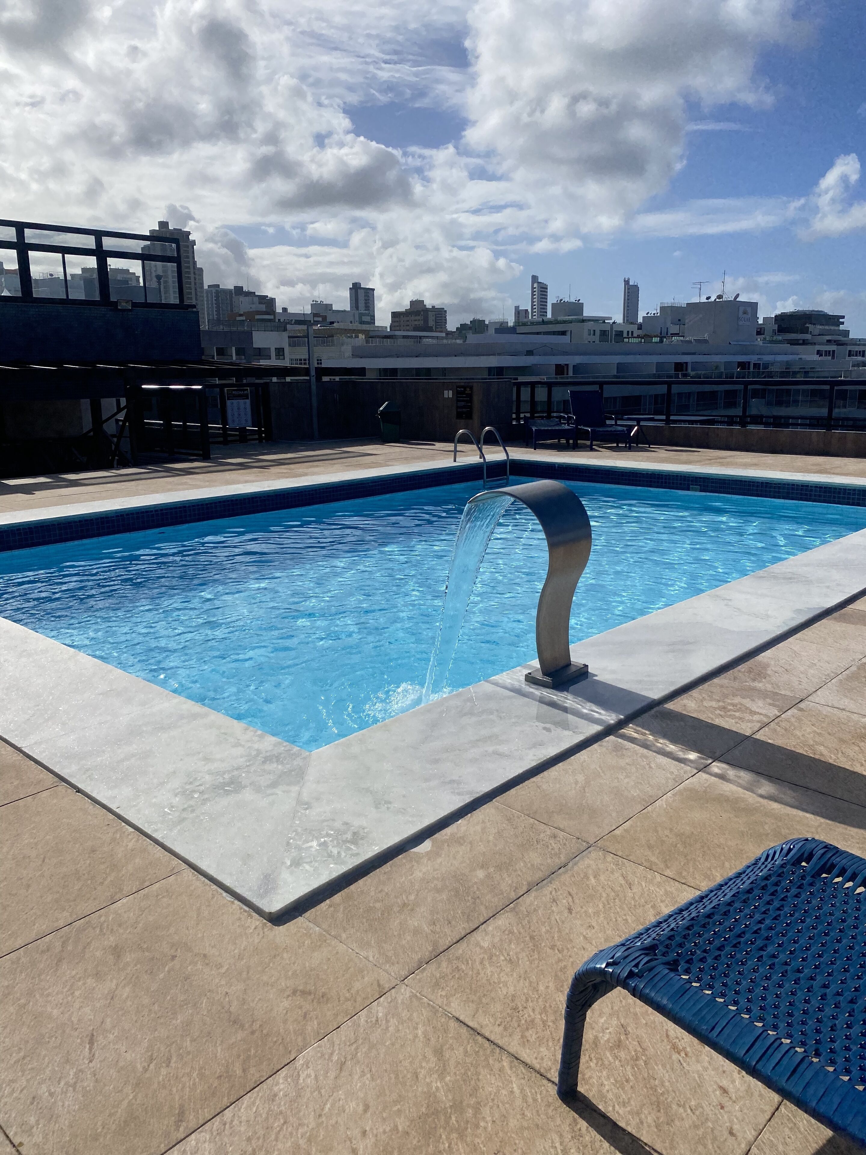 Una piscina en la azotea con un cielo azul despejado y edificios de la ciudad al fondo.