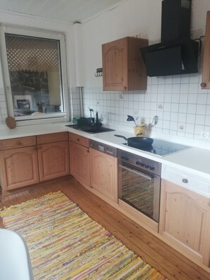 A kitchen with wooden cabinets, a black range hood, a dishwasher, and a window with a decorative screen.