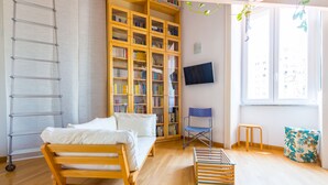 A room with a wooden bed, a bookshelf, a TV, and a window with a view of buildings. - Montemiletto a Panoramic Nest by Napoliapartments (Napoli)