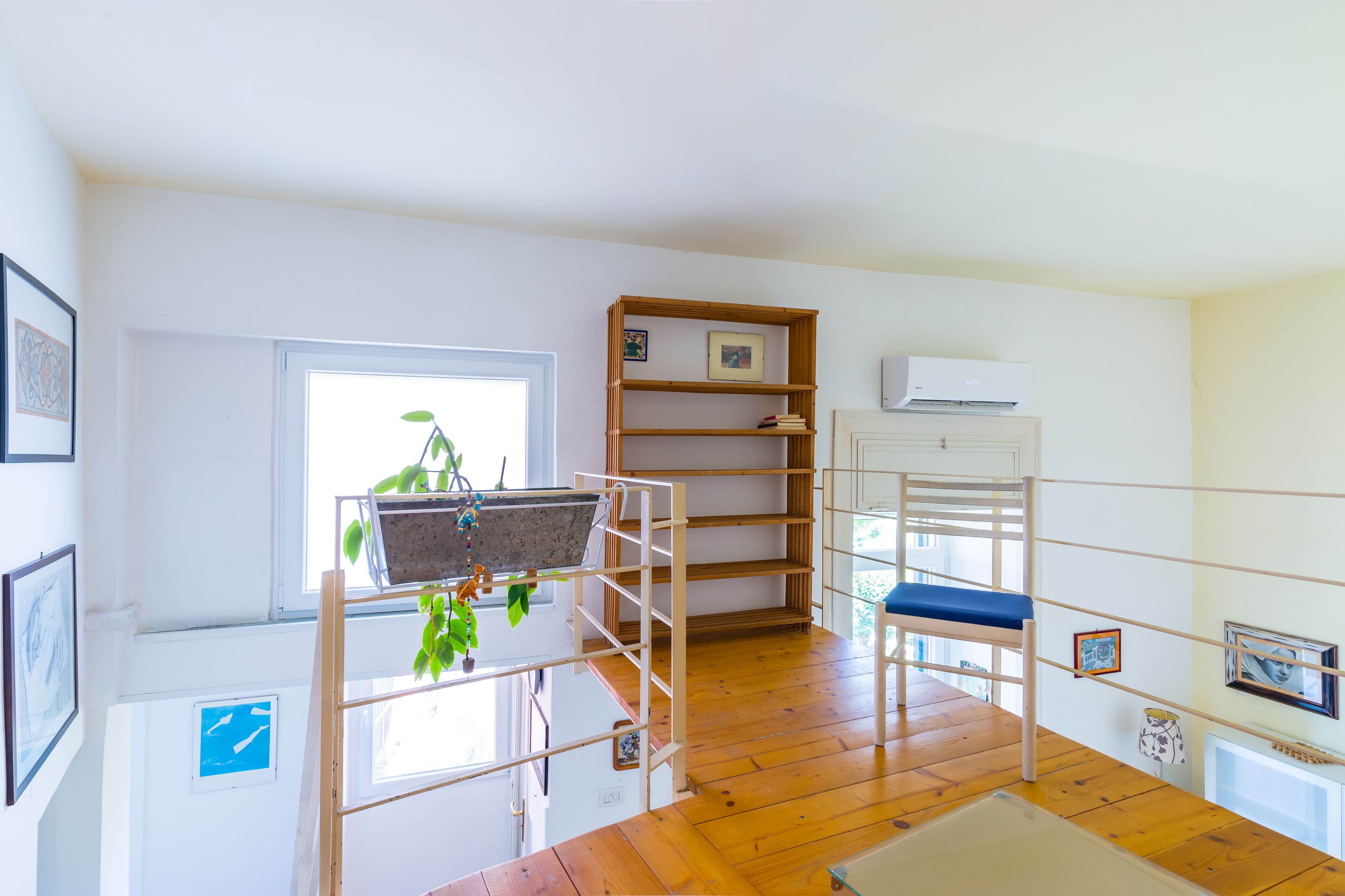A room with a bunk bed, a desk, a chair, a window with a plant, and a shelf with framed pictures.