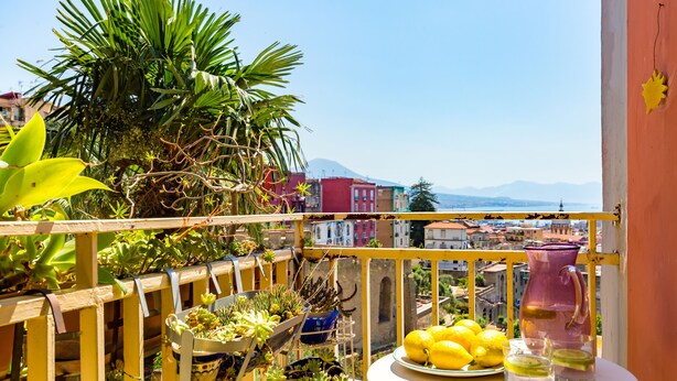 A balcony with potted plants, a table with lemons and drinks, and a view of buildings and mountains. - Montemiletto a Panoramic Nest by Napoliapartments (Napoli)
