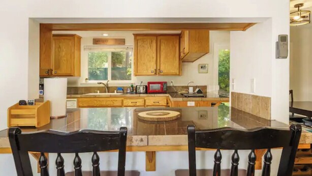 Una cocina con armarios de madera, una isla central con sillas, un microondas y un ventanal con vistas al verdor.