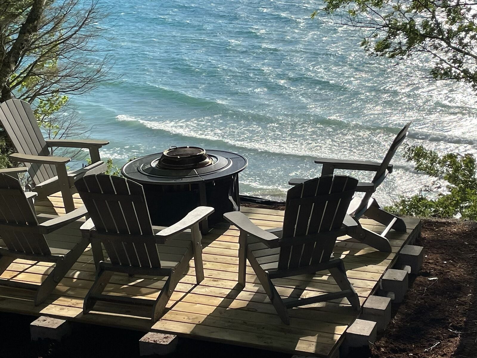 A deck with Adirondack chairs and a round table overlooking the ocean.