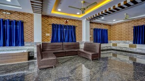 A modern lobby with a sectional sofa, blue curtains, a brick wall, and a polished granite floor. - Itsy Hotels Galaxy Park (Hyderabad)