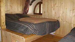 A bed with a striped mattress and a brown blanket in a wooden room with a window and a curved wall. - Chalet 16personnes - Orellette (Orellette)
