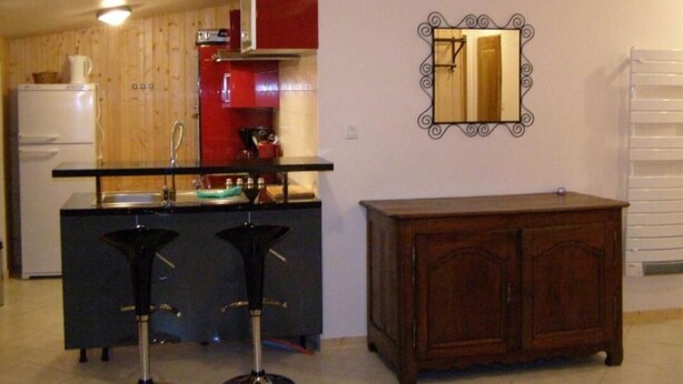 A kitchen with a wooden cabinet, a red appliance, a black bar stool, and a wooden cabinet. - Chalet 16personnes - Orellette (Orellette)