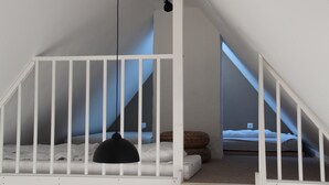 Un dormitorio con techo inclinado, una cuna blanca, una lámpara colgante negra y una cama con cabecero marrón.