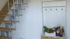 Un interior moderno con una escalera de madera, un armario blanco montado en la pared con ganchos y una lámpara colgante.